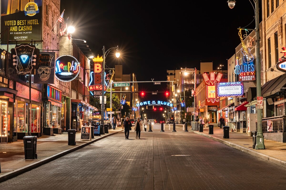 A nighttime view of Beale Street in Memphis, lined with neon signs, bars, and restaurants, with a few people walking along the street—once home to legends like the Memphis Jug Band and celebrated during Black History Month.