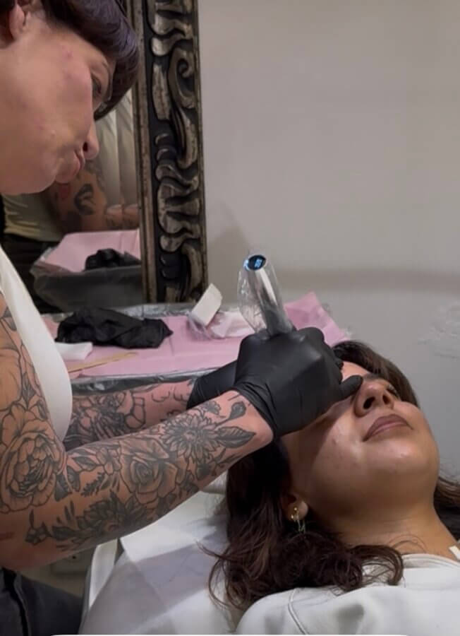This Master Memphis Tattoo Artist Helps Women Feel Whole Again - 3 A tattoo artist from FACES with floral tattoos and black gloves works on a woman’s eyebrow as she lies on a table in Nicolette Tomblyn’s studio.