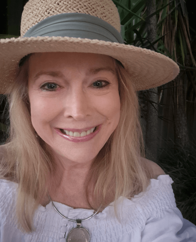 Patricia Gordon Stevens, featured in FACES, smiles at the camera outdoors, her long blonde hair flowing under a straw hat and white off-shoulder top.