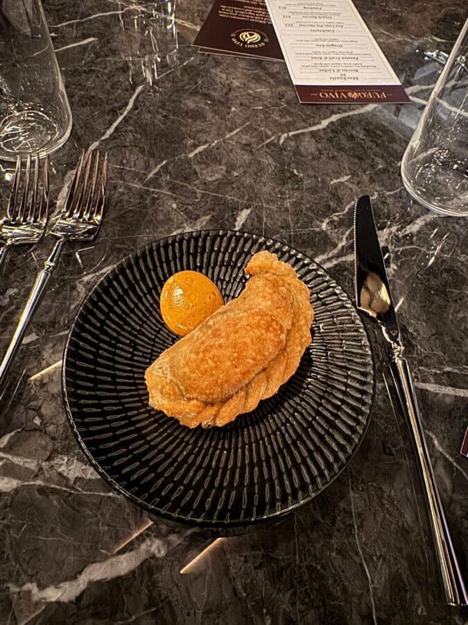 5 New Memphis Restaurants to Try This Month (+ What's Coming Soon!) - 13 A single fried empanada with a dollop of orange sauce on a black plate, set on a marble table with silverware and glasses.