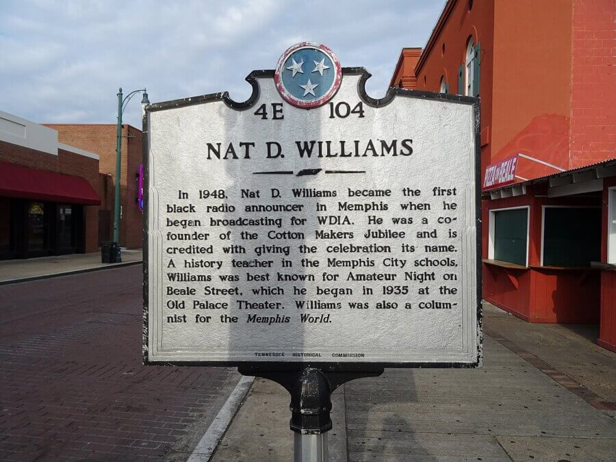 A historical marker on a sidewalk describes Nat D. Williams, noting his achievements as a radio announcer on WDIA Radio and teacher in Memphis, Tennessee.