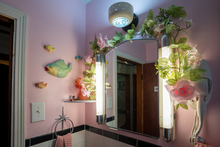 Lil' Graceland: An Elvis-Inspired Retreat Just Minutes from the Real Deal - 8 A bathroom with pink walls, a mirror framed by artificial flowers, fish and bird wall decorations, a wall-mounted hairdryer, and a towel on a star-shaped holder.