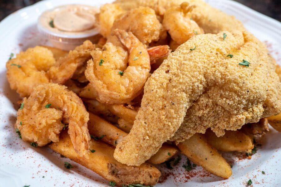 A plate of fried fish, breaded shrimp, and thick-cut fries garnished with herbs, served with a cup of dipping sauce—a true taste of Mississippi soul food.