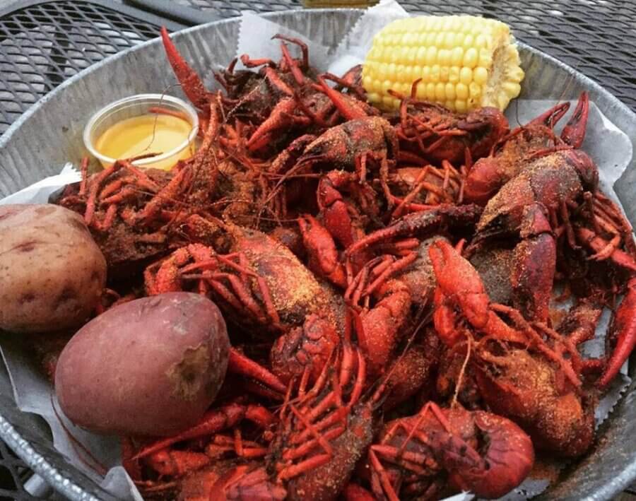 2026 Memphis Crawfish Season Guide - 3 A metal tray filled with seasoned boiled crawfish, two red potatoes, a piece of corn on the cob, and a cup of dipping sauce.