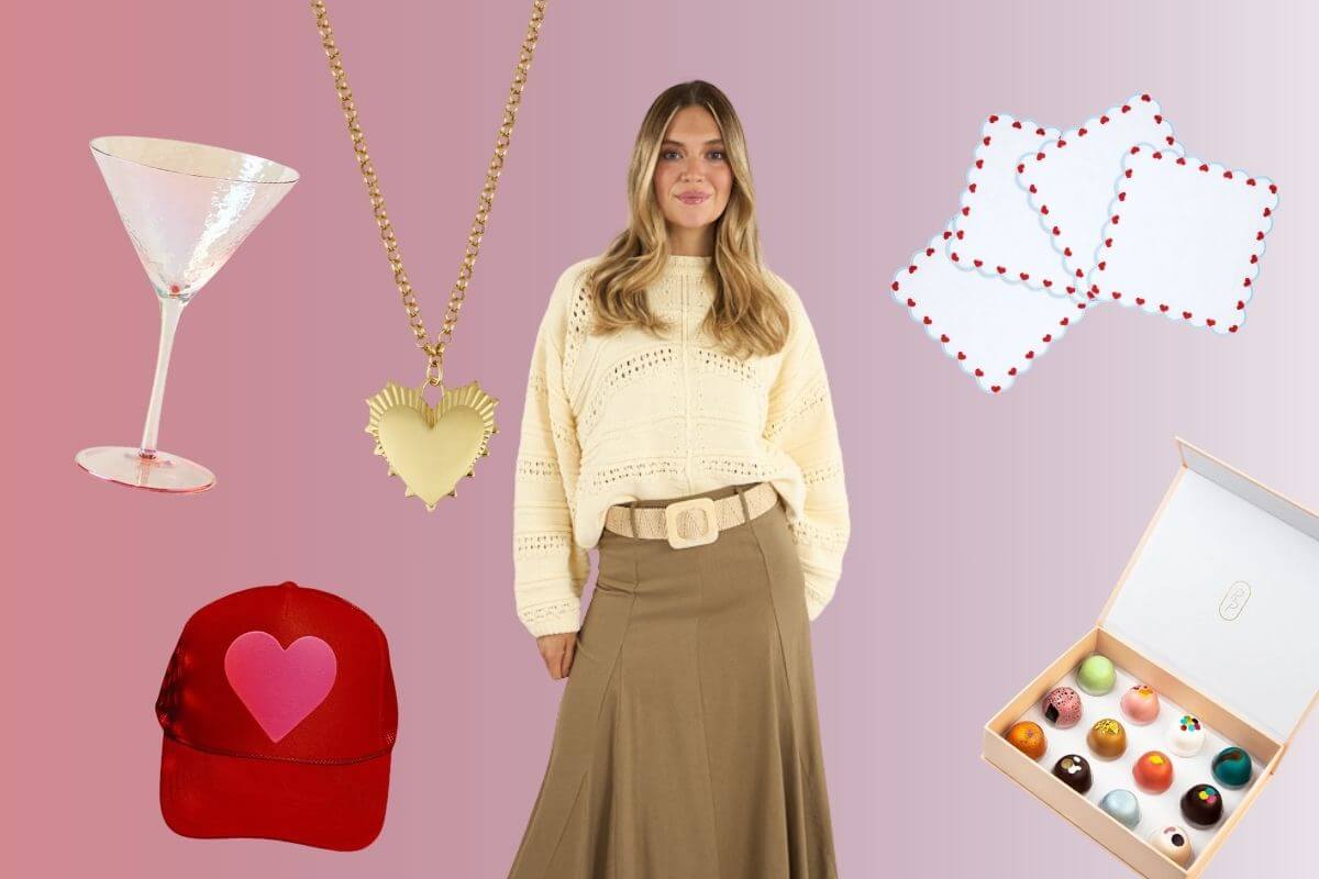A woman in a cream sweater and tan skirt stands surrounded by valentines day gifts—a martini glass, heart necklace, red cap, coasters, and a box of chocolates—on a pink gradient background.