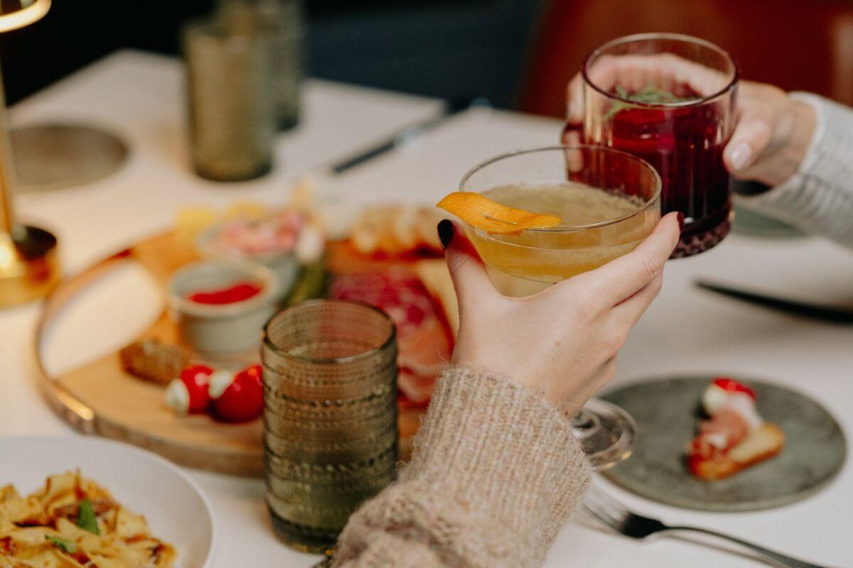 Two people clink cocktail glasses over a table with assorted snacks, including a charcuterie board, enjoying the vibrant atmosphere of new Memphis restaurants.