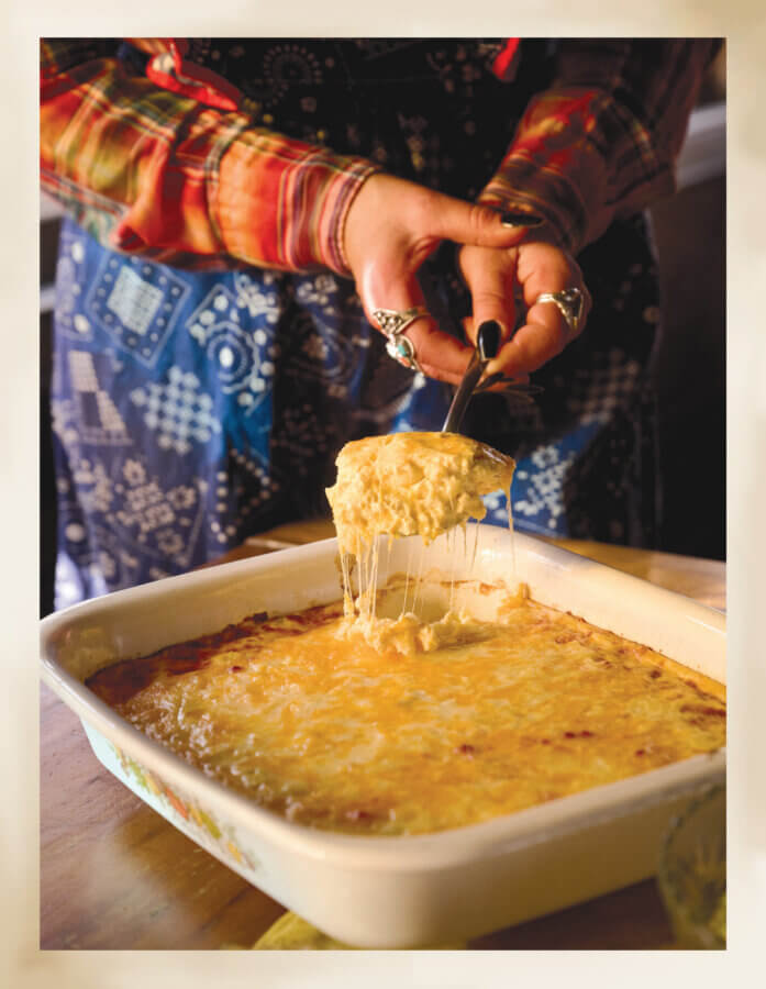 RECIPE: Getchyo' Man Macaroni Cheese - 2 A person serves a cheesy casserole from a baking dish, with melted cheese stretching from the serving utensil.