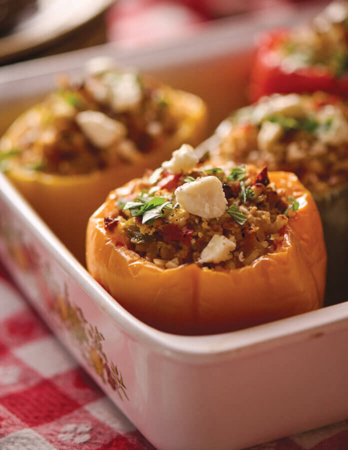 RECIPE: Keep Yo' Man Stuffed Peppers - 2 Close-up of stuffed bell peppers filled with rice, vegetables, and herbs, topped with crumbled cheese, in a white baking dish on a red and white checkered tablecloth.