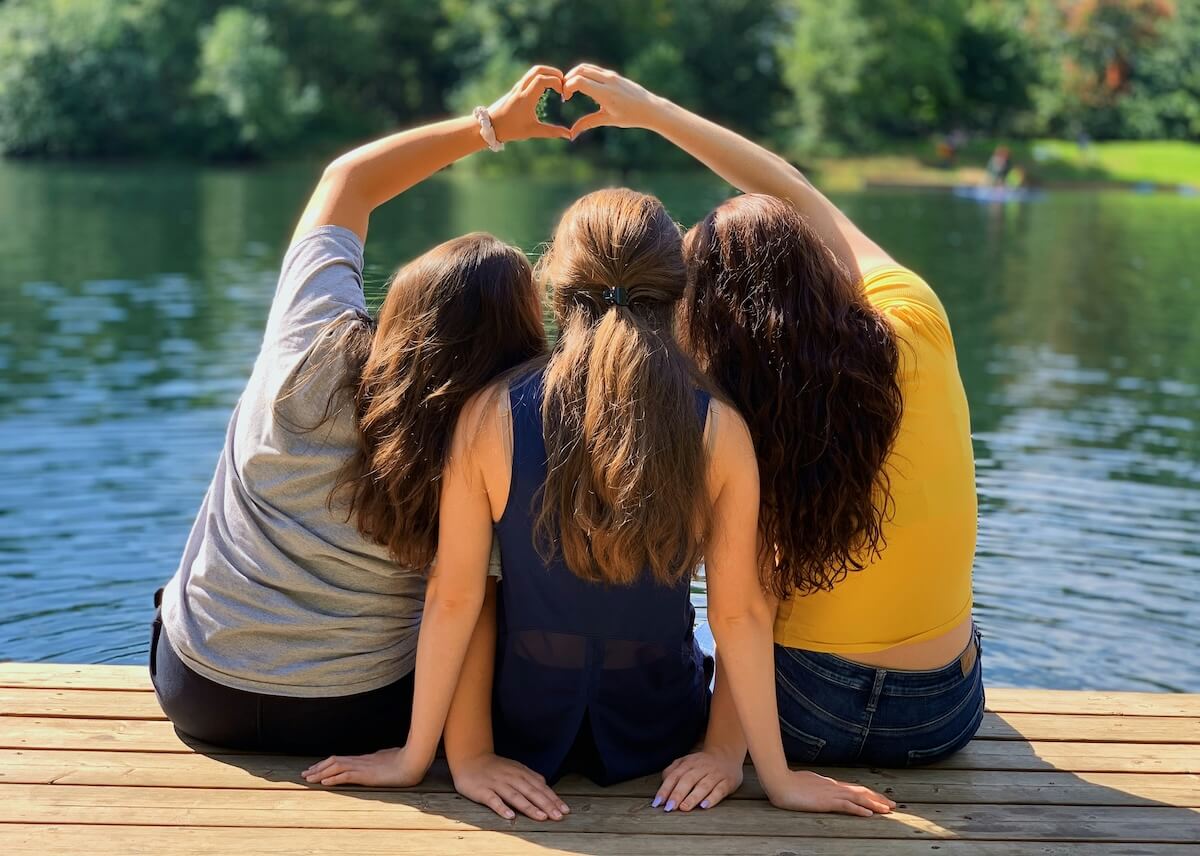A group of people sitting on a dock at summer camp, making a heart with their hands and creating lifelong memories.