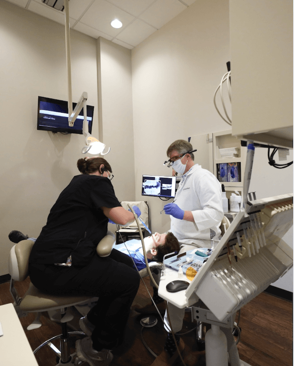 Nashville Steals, Deals & Announcements: March 2026 - 4 A dentist and an assistant perform a dental procedure on a patient in a modern dental clinic, with monitors displaying X-ray images in the background.