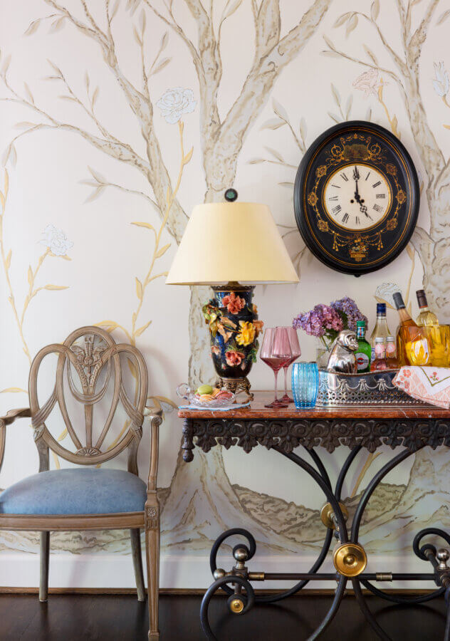 Something Old, Something New: How Ellie Christopher Makes Antiques Feel Fresh - 3 A chair with a blue cushion next to a table with a colorful lamp and bar cart with a clock on the wall.