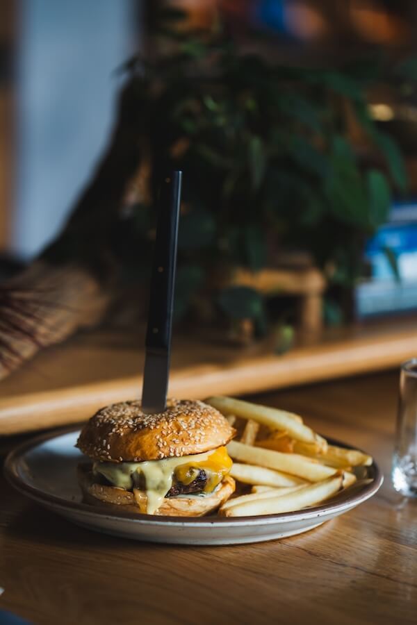 A cheeseburger with a knife stuck through the middle is served on a plate with a side of French fries, perfect for classic bar dining Nashville style.