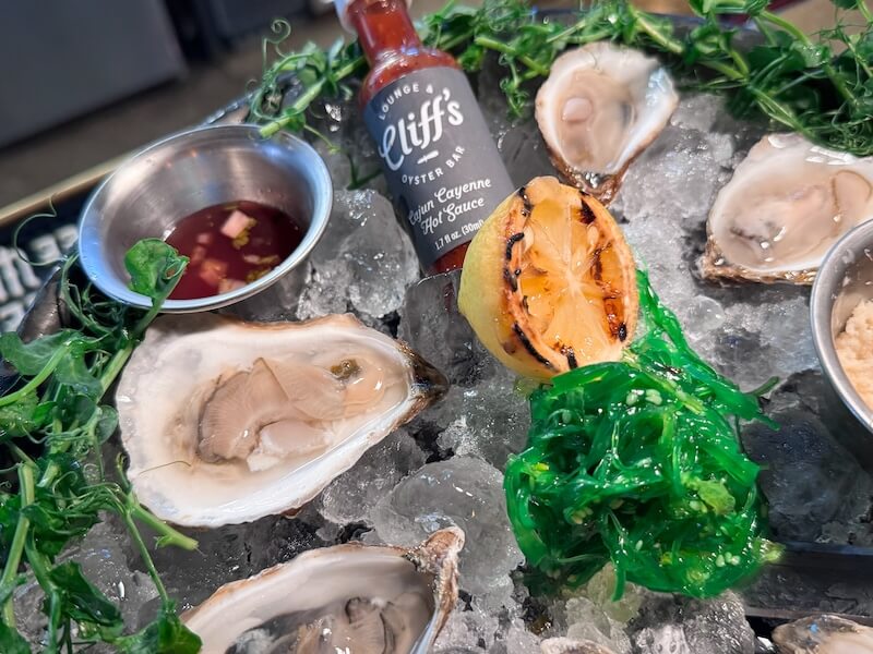 20 Epic Spots to Grab Dinner at the Bar in Nashville - 5 A plate of raw oysters on ice with a grilled lemon, green garnish, hot sauce, and condiments—perfect for dinner at the bar.