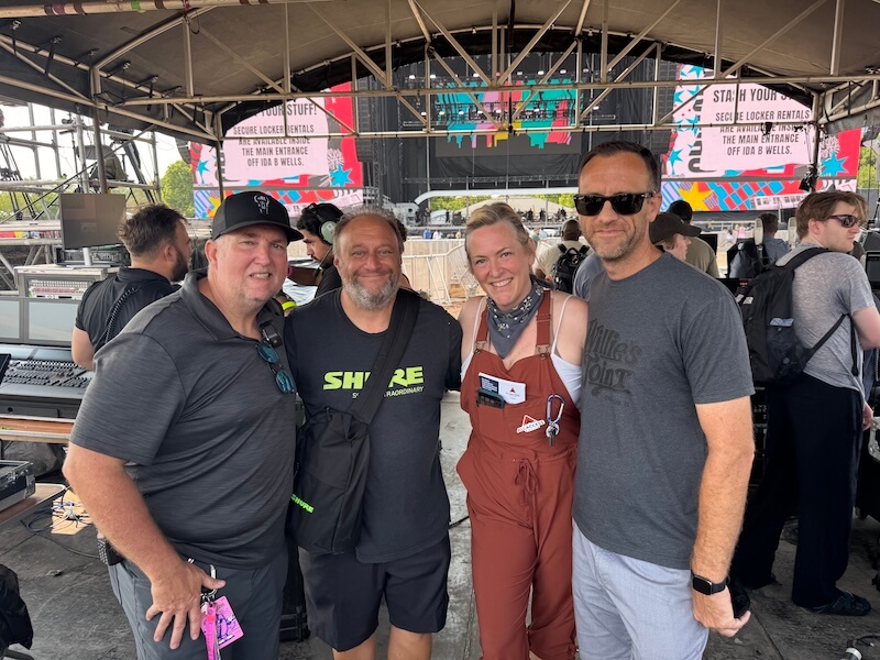 She's Building a Support Network for Nashville's Live Music Community - 3 Four people, including Kara Kemp, stand together smiling on an outdoor stage with audio equipment and colorful signs in the background.