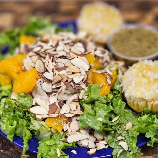 Enjoy a fresh plate of green lettuce with mandarin orange slices and sliced almonds, served with two muffins and green dressing—a delicious option inspired by new restaurants coming to Nashville in February 2026.