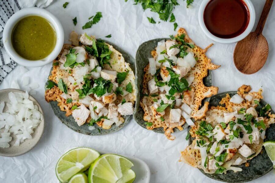 Three blue corn tacos topped with grilled chicken, chopped onions, and cilantro are surrounded by lime wedges, green and red sauces, and a small bowl of diced onions—a must-try at one of the best new Nashville restaurants.