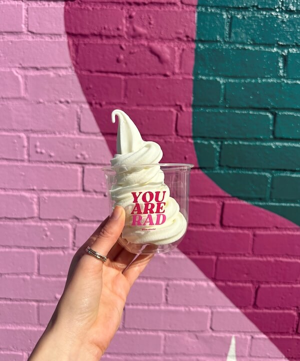 Hand holding a cup of soft-serve ice cream with "YOU ARE RAD" written on it, in front of a colorful, painted brick wall—perfect for discovering new restaurants in Nashville this February 2026.