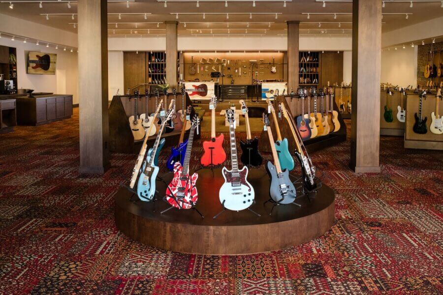 9 New Nashville Retail Spots to Explore - 2 A display of electric and acoustic guitars arranged on stands in a showroom with wooden columns and patterned carpet showcases the vibe of new retail in Nashville.