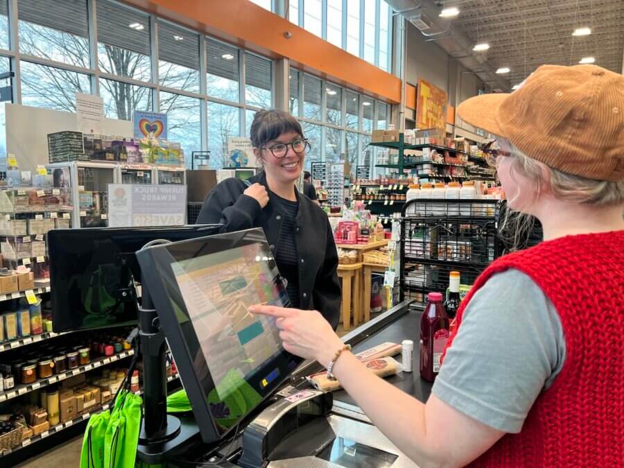 Turnip Truck & 'The Store' Are Rounding Up for Neighbors in Need - 3 A cashier at the store rings up groceries, including a fresh turnip truck delivery, while engaging in friendly conversation with the customer at checkout.