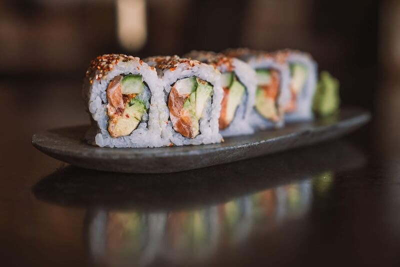 Sushi in Nashville is a THING. Here's Your Guide. - 5 A close-up of sushi rolls filled with avocado and fish, arranged in a row on a dark rectangular plate with a small portion of wasabi on the side, captures the fresh flavors of Nashville’s vibrant sushi scene.