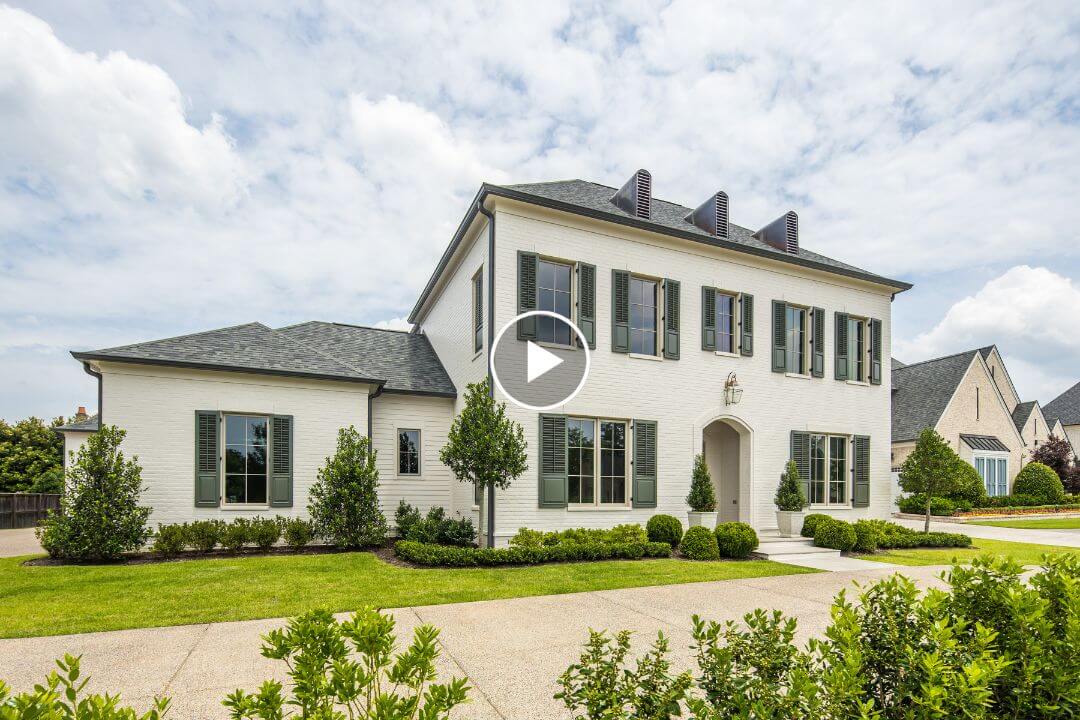 A two-story white brick house with green shutters, black roof, manicured lawn, shrubs, and driveway under a partly cloudy sky in the desirable Chapel Woods neighborhood of Germantown, TN.