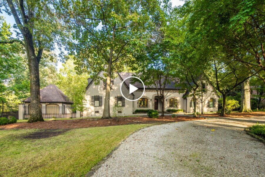 Large two-story house with light-colored exterior at 704 W Clover Dr, Memphis TN, surrounded by tall trees and greenery, with a gravel driveway curving toward the entrance on a sunny day.