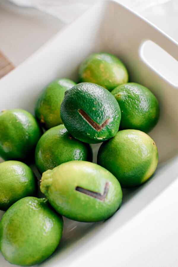 Rustic Meets Romance in This Texas Hill Country Wedding - 7 A white rectangular dish containing several whole limes, two of which have dark check mark symbols etched into their skin—perfect for adding a unique touch to your rustic wedding décor.