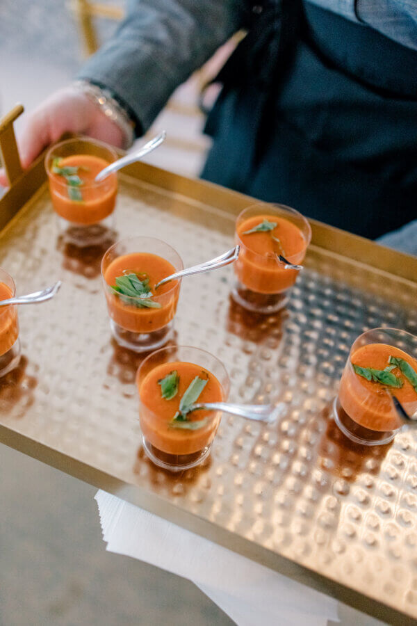 Rustic Meets Romance in This Texas Hill Country Wedding - 13 Six small glasses of tomato soup, each garnished with herbs and served with a spoon, are arranged on a gold tray held by a person at a Hill Country wedding in Fredericksburg, Texas.