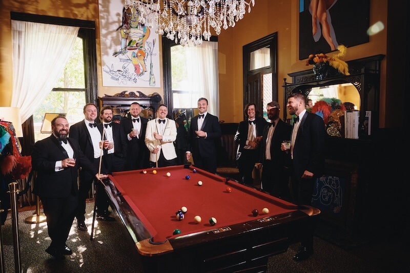 A Dreamy Disco Wedding at The Columns NOLA - 5 A group of men in tuxedos standing around a pool table, ready to celebrate at a disco wedding.
