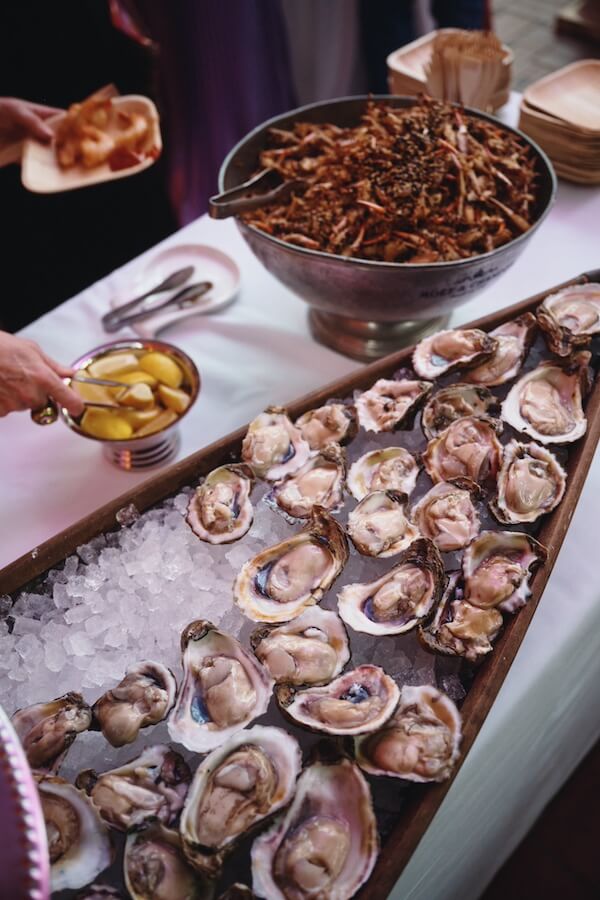 A Dreamy Disco Wedding at The Columns NOLA - 10 A display of fresh oysters on ice, a bowl of lemon wedges, and a large bowl of fried food are arranged on a table at a lively disco wedding catering event.