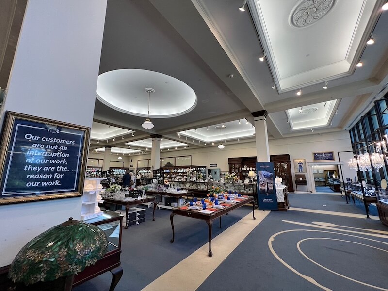 Where the "Good China" Lives: Inside Replacements, Ltd. - 3 Spacious retail store interior with display tables of various products, large windows, high ceilings, and a framed sign about customer service on the left wall—perfect for browsing Replacements Ltd’s selection of Good China.