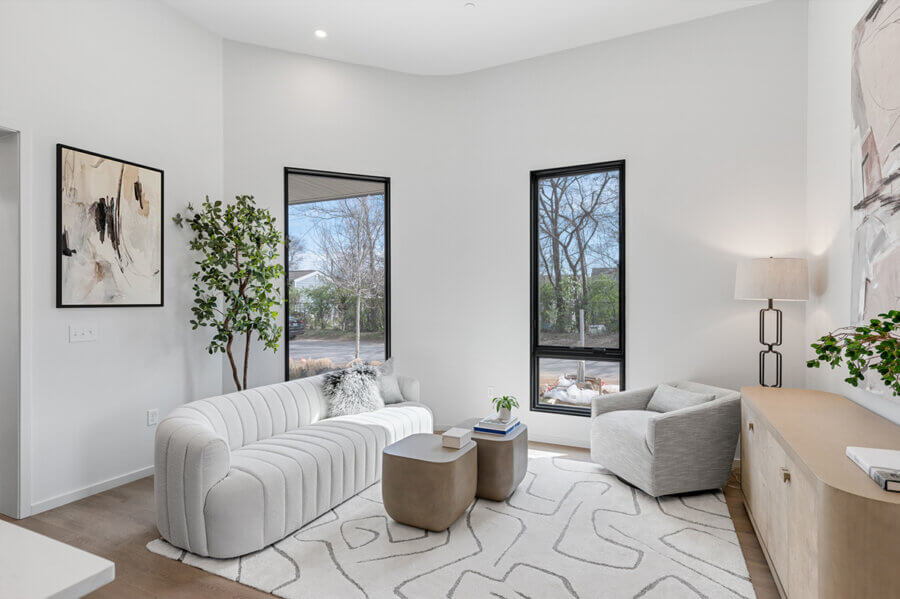 Modern living room at 506 Merritt Ave, Nashville, featuring a white sofa, gray armchair, two coffee tables, large windows, abstract art, and neutral decor.