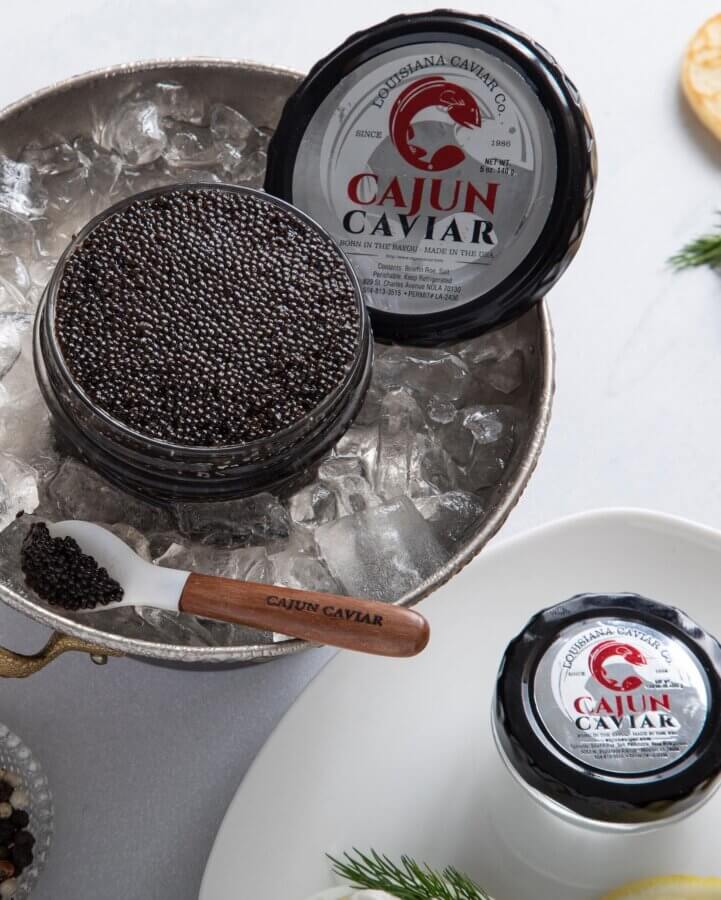 Un pot ouvert de Cajun Caviar, une marque remarquable parmi les marques de caviar du Sud, repose sur la glace à côté d'un pot fermé. Une petite cuillère étiquetée 
