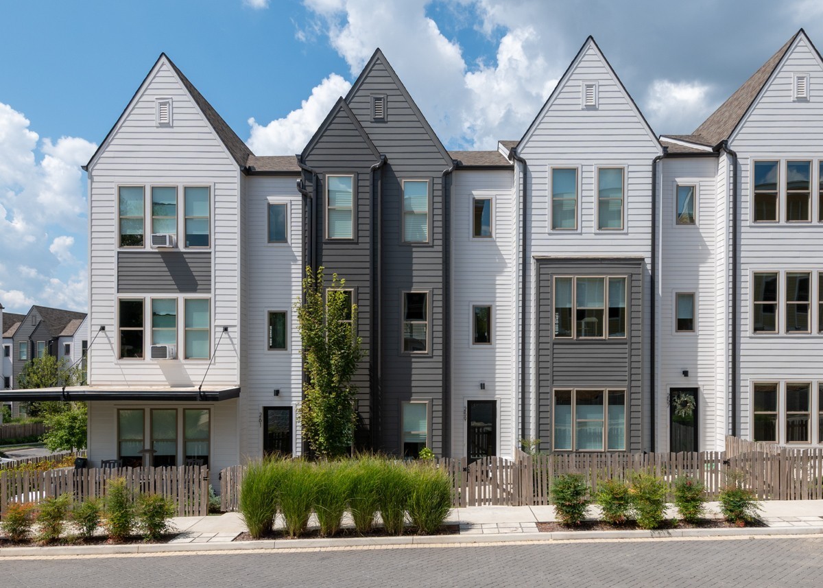 Modern three-story townhouses on 257 Arrowhead Dr, Nashville TN, feature light and dark gray siding, large windows, small front yards, and a picket fence along a suburban street under a partly cloudy sky.