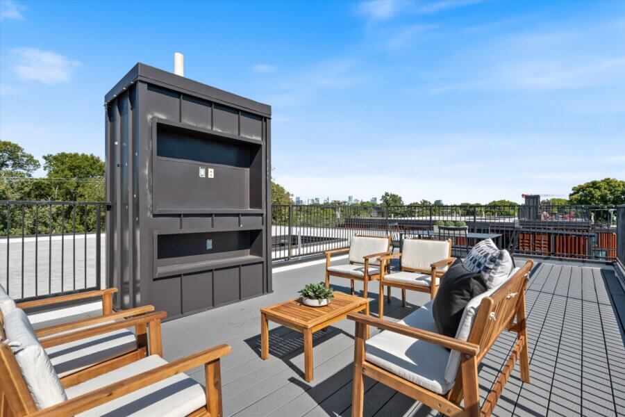 Rooftop patio at 2140 Byrum Ave, Nashville, TN, featuring four wooden chairs, a small table, and a built-in outdoor structure—perfectly framed by a black metal railing with scenic views of trees and sky.
