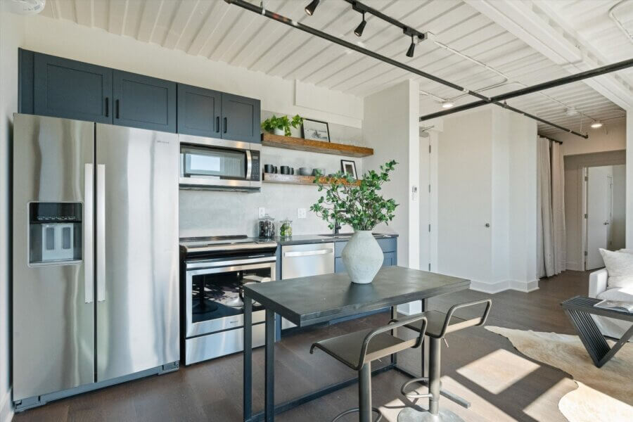 Modern kitchen at 2140 Byrum Ave, Nashville, TN with stainless steel appliances, black cabinets, open shelves, a black dining table for two, and a vase with greenery as the centerpiece.