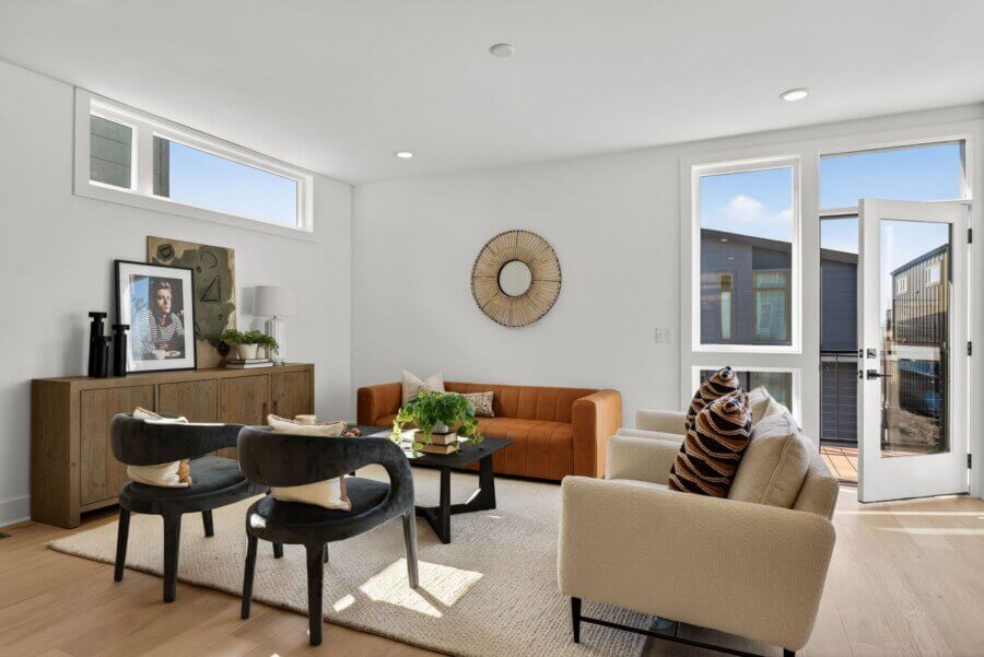 Modern living room at 3017 Edwin Circle, Nashville, with a tan sofa, beige armchair, two black chairs, wooden sideboard, coffee table with plants, wall mirror, and an open door leading to the outdoor area.
