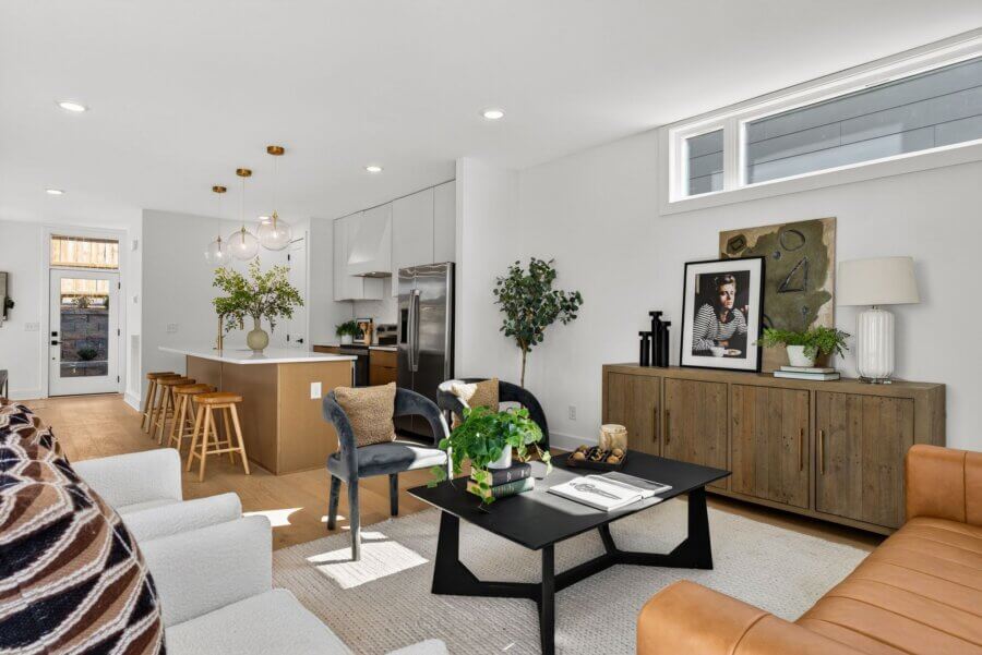 Modern open-concept living room and kitchen at 3017 Edwin Circle, Nashville TN, featuring neutral tones, wood accents, plants, a kitchen island with stools, and abundant natural light from large windows.