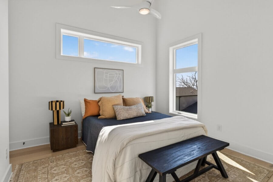 A modern Nashville bedroom at 3017 Edwin Circle features white walls, a bed with dark blue bedding and tan pillows, two bedside tables with lamps, and a black bench at the foot of the bed.