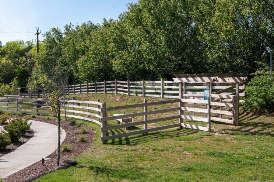A wooden fence encloses a grassy area next to a sidewalk on 257 Arrowhead Dr, Nashville, with a signpost and trees in the background on a sunny day.
