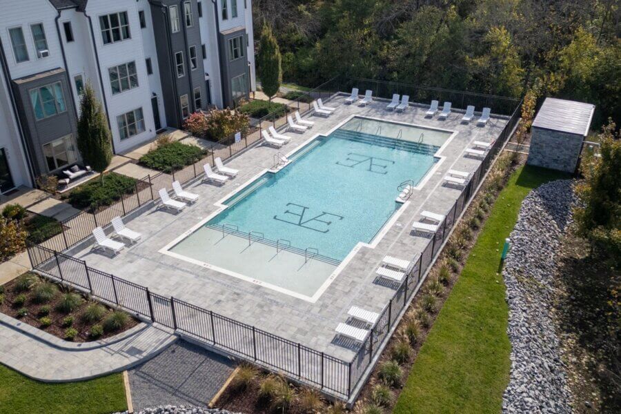 A rectangular outdoor swimming pool with lounge chairs and umbrellas, surrounded by a fence, sits beside a modern apartment building and landscaped areas at 257 Arrowhead Dr, Nashville.