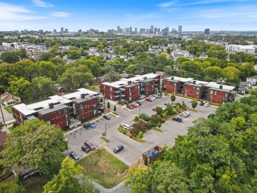 Aerial view of a residential apartment complex with parking lot, surrounded by trees and houses near 2140 Byrum Ave, Nashville, with a city skyline in the background under a blue sky.