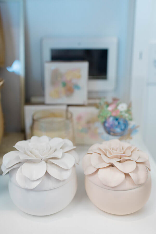 15 Memphis FINDS at Local Shops: Spring Dresses, Home Decor & More! - 13 Two round ceramic containers with sculpted floral lids, one white and one light pink, sit side by side on a shelfβunique Memphis FINDS for Marchβadding charm among the decorative items in the background.