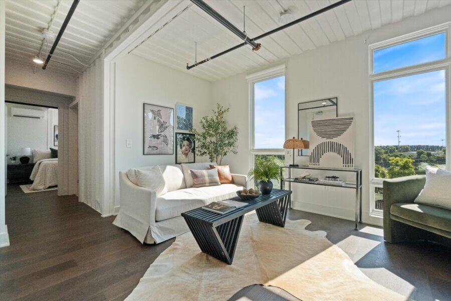 Modern living room at 2140 Byrum Ave, Nashville TN, featuring a white sofa, black coffee table, cowhide rug, wall art, and large windows. Natural light fills the space and offers a partial view of the bedroom.