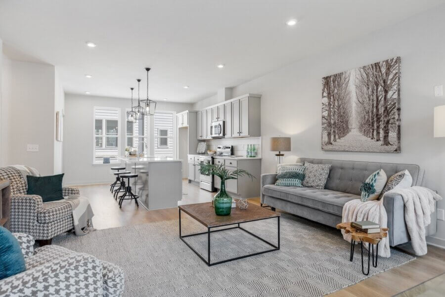 Modern open-concept living room and kitchen at 257 Arrowhead Dr, Nashville, featuring neutral tones, gray sofa, armchairs, large wall art, island with stools, wooden floors, and contemporary decor.