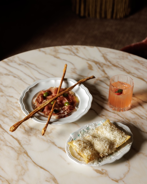 A marble table at one of the new Nashville restaurants features a plate of cured meat and breadsticks, ravioli topped with cheese, and a glass of pink cocktail.