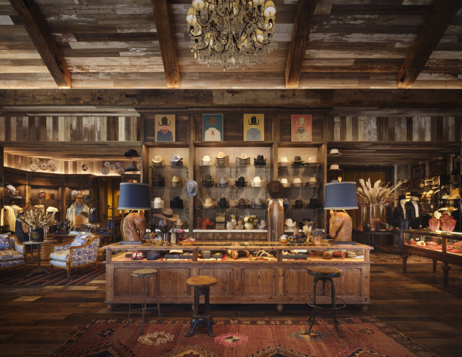 Kendra Scott's Latest Concept Has Landed in Nashville: Apparel, Craft Cocktails & More - 2 Rustic boutique interior with wooden beams, hats displayed on shelves, Western-themed decor, a chandelier, and a central wooden counter with stools and lamps.