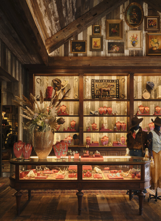 Kendra Scott's Latest Concept Has Landed in Nashville: Apparel, Craft Cocktails & More - 4 A rustic boutique displays jewelry in glass cases and on shelves, with hats and mannequin torsos in western attire; floral art hangs on wood-paneled walls.