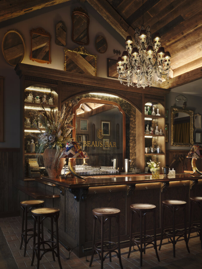 Kendra Scott's Latest Concept Has Landed in Nashville: Apparel, Craft Cocktails & More - 6 A rustic bar with wooden stools, vintage decor, a chandelier, mirrors on the wall, and "Beau's Bar" written on a large mirror behind the counter.