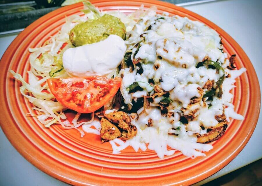 9 New Birmingham Restaurants to Try This Month - 9 A plate with shredded chicken and melted cheese, sliced lettuce, a tomato wedge, guacamole, and sour cream on an orange dish—perfect for sampling the flavors found at new restaurants in Birmingham.